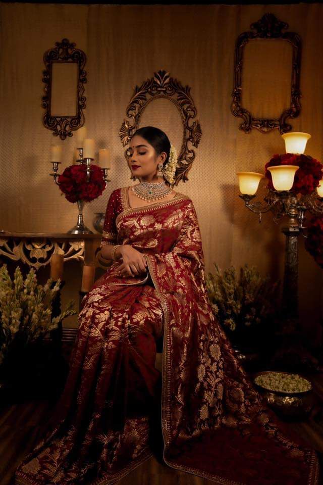 a woman in a red and gold sari sitting on a chair with candles behind her