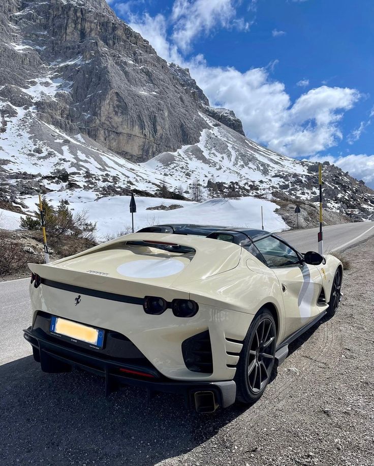 a white sports car parked on the side of a road in front of a mountain