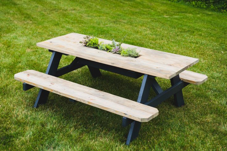 a wooden picnic table with two benches in the grass next to it and a potted plant on top