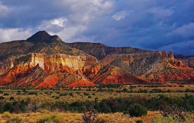 the mountains are covered in red, orange and yellow rock formations under a cloudy sky