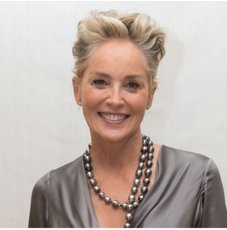 a woman wearing a necklace with pearls on it and smiling at the camera while standing in front of a white wall