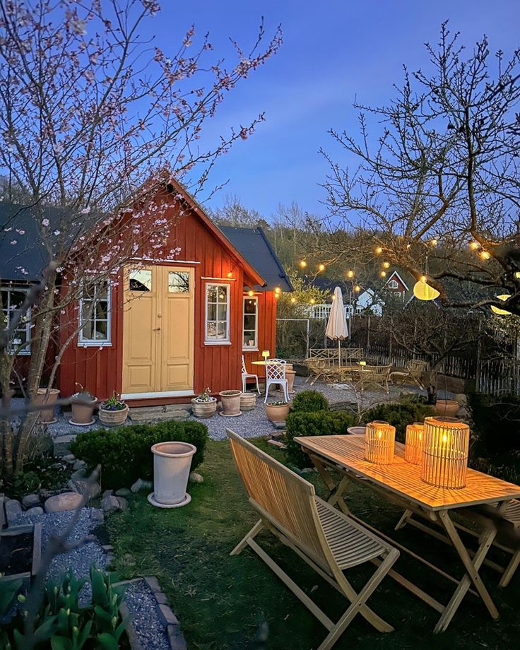 an outdoor dining area with wooden tables and chairs in front of a small red house