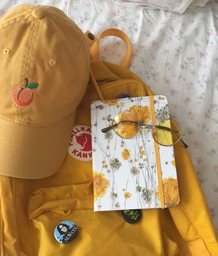 a yellow backpack with a notepad and glasses on it, next to a hat