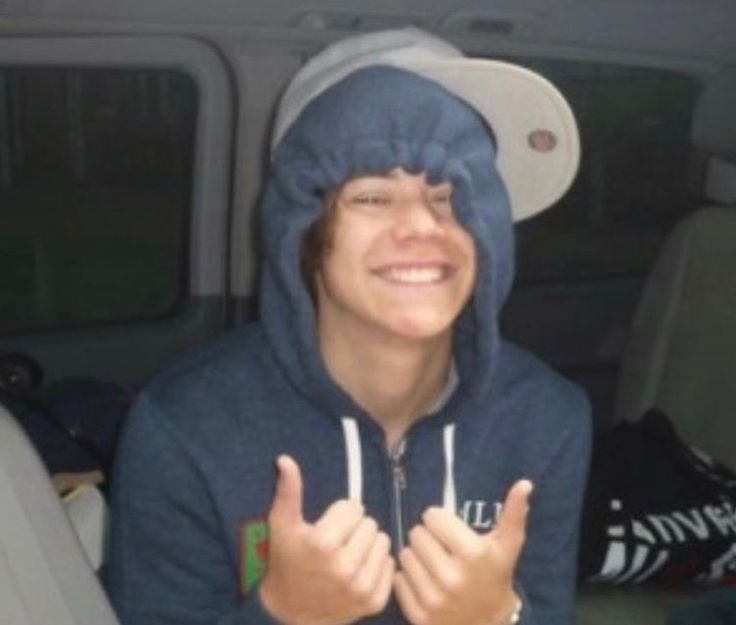 a man in a blue hoodie giving the thumbs up sign while sitting in a car