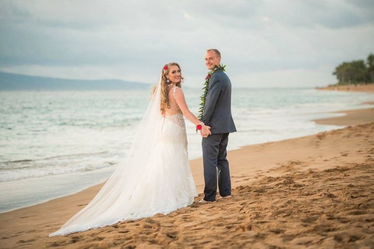 a bride and groom standing on the beach