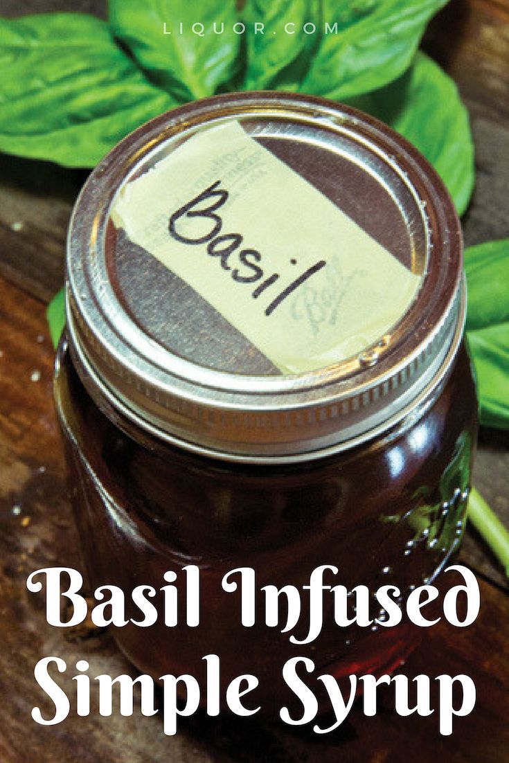 basil infused simple syrup in a glass jar on top of a wooden table next to fresh basil leaves