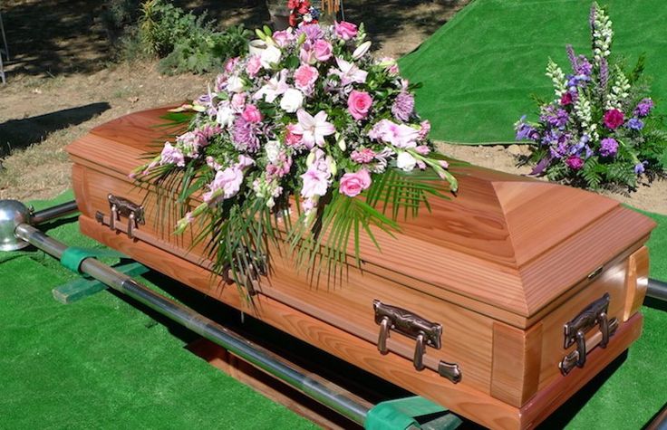 a wooden casket sitting on top of a green grass covered field next to purple and white flowers