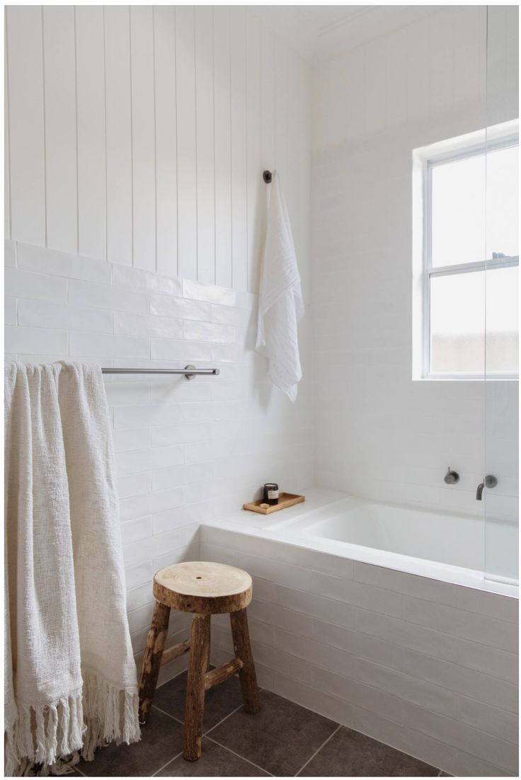 a white bath tub sitting under a window next to a wooden stool in a bathroom