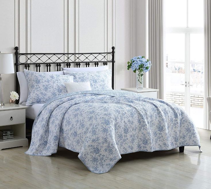 a bed with blue flowers on it in a room next to a white dresser and window