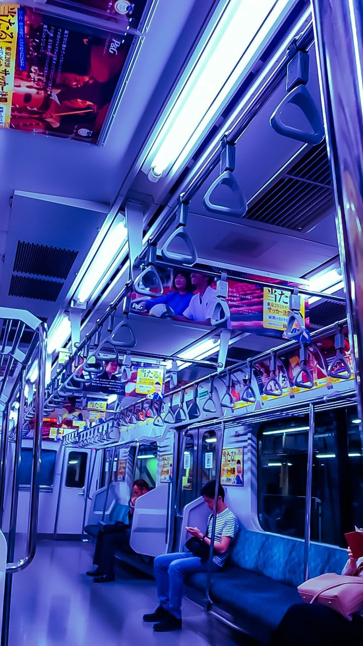 two people sitting on a subway car with their backs turned to the side, looking at their cell phones