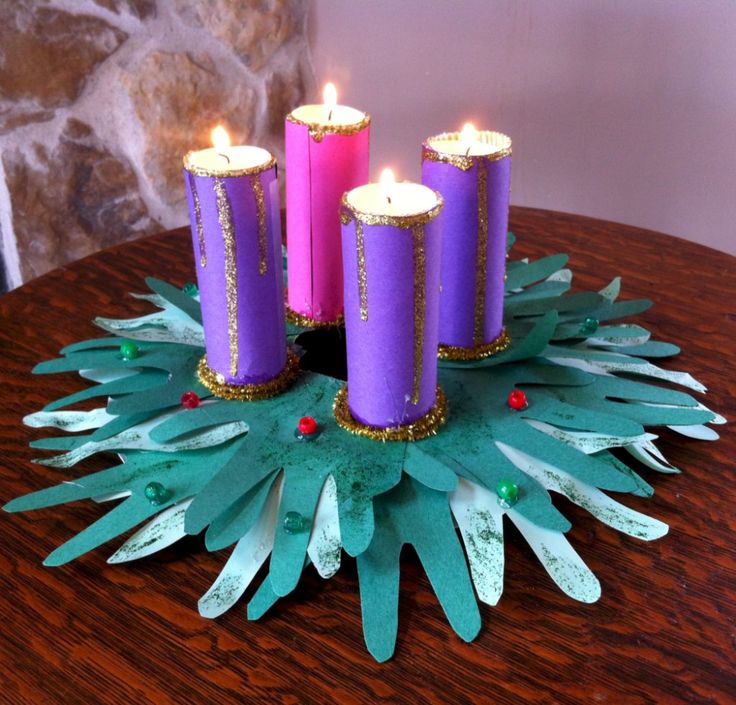 three purple candles are sitting on top of a green paper wreath with pineconis