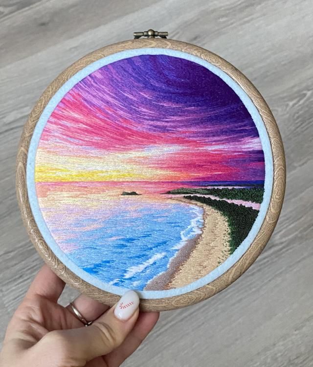 someone is holding up a colorful painting on a piece of wood that has been stitched to it