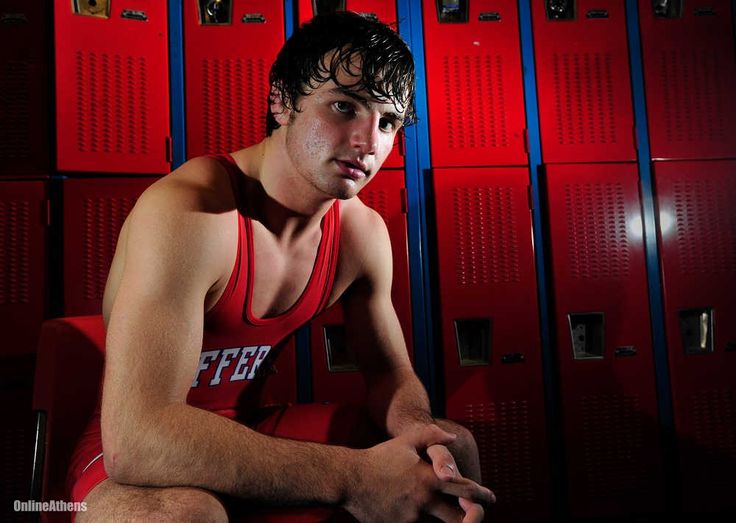 a young man sitting in front of lockers with his hands on his knees looking at the camera