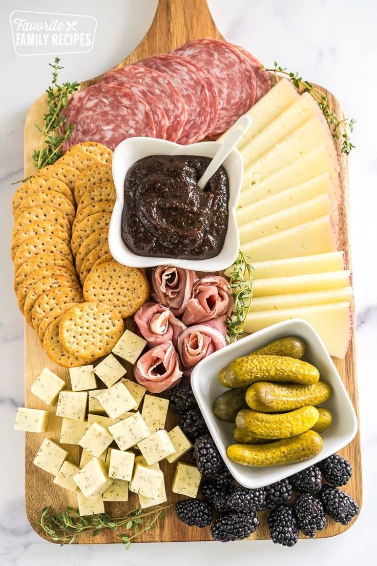 an assortment of cheeses, crackers, and pickles on a cutting board