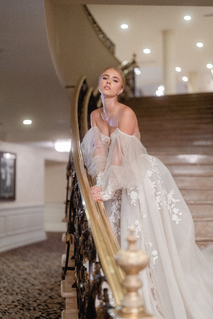 a woman in a white dress is standing on a stair case with her hand on the railing