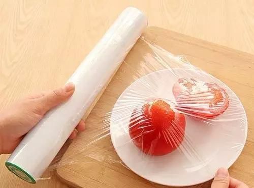 a person holding a plastic wrapper over a tomato on a plate