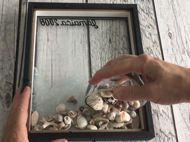 a person holding a glass jar filled with seashells on top of a wooden table