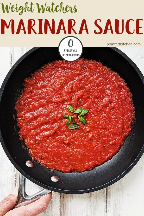 a skillet filled with marinara sauce on top of a white wooden table next to a person's hand