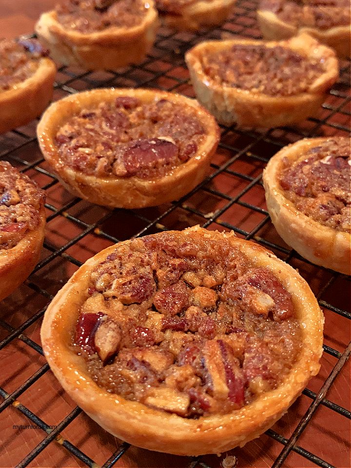 several small pies cooling on a rack with some nuts in the middle and one is topped with cranberry sauce