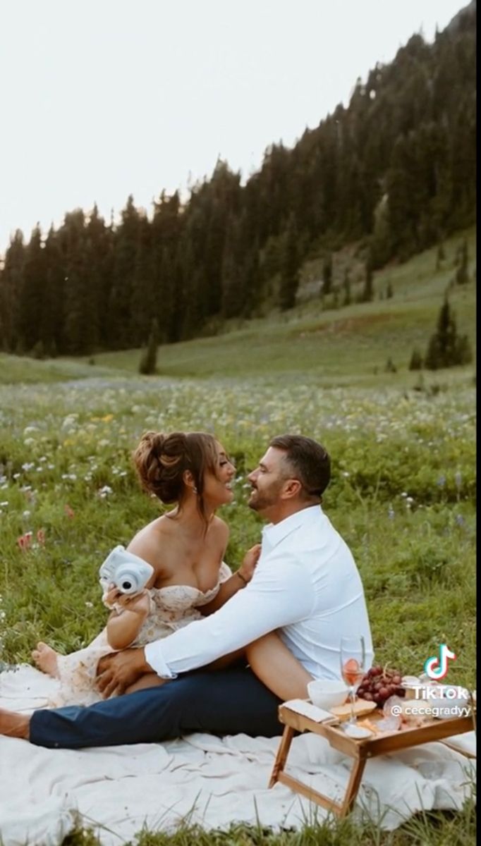 a man and woman sitting on a blanket in the grass