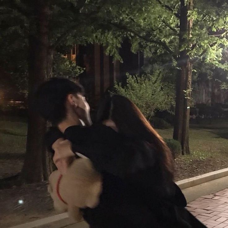 a man and woman kissing in front of trees at night with lights shining on them