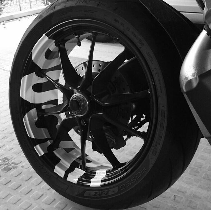 black and white photo of the front wheel of a motorbike on brick pavement