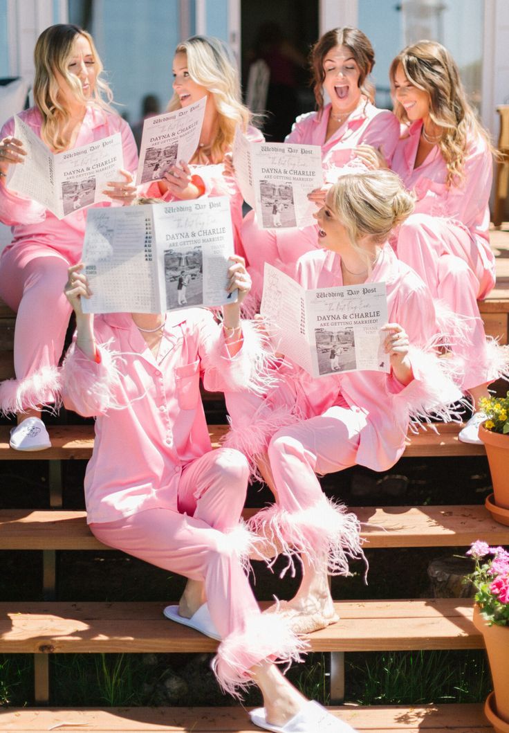 a group of women in pink pajamas sitting on some steps reading paper and smiling at the camera