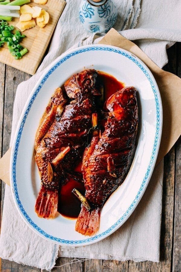 a white plate topped with cooked fish on top of a wooden table next to vegetables