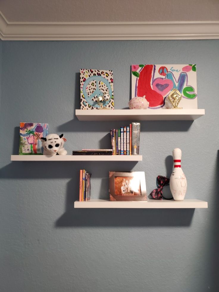 two white shelves with books and toys on them against a blue wall in a child's room