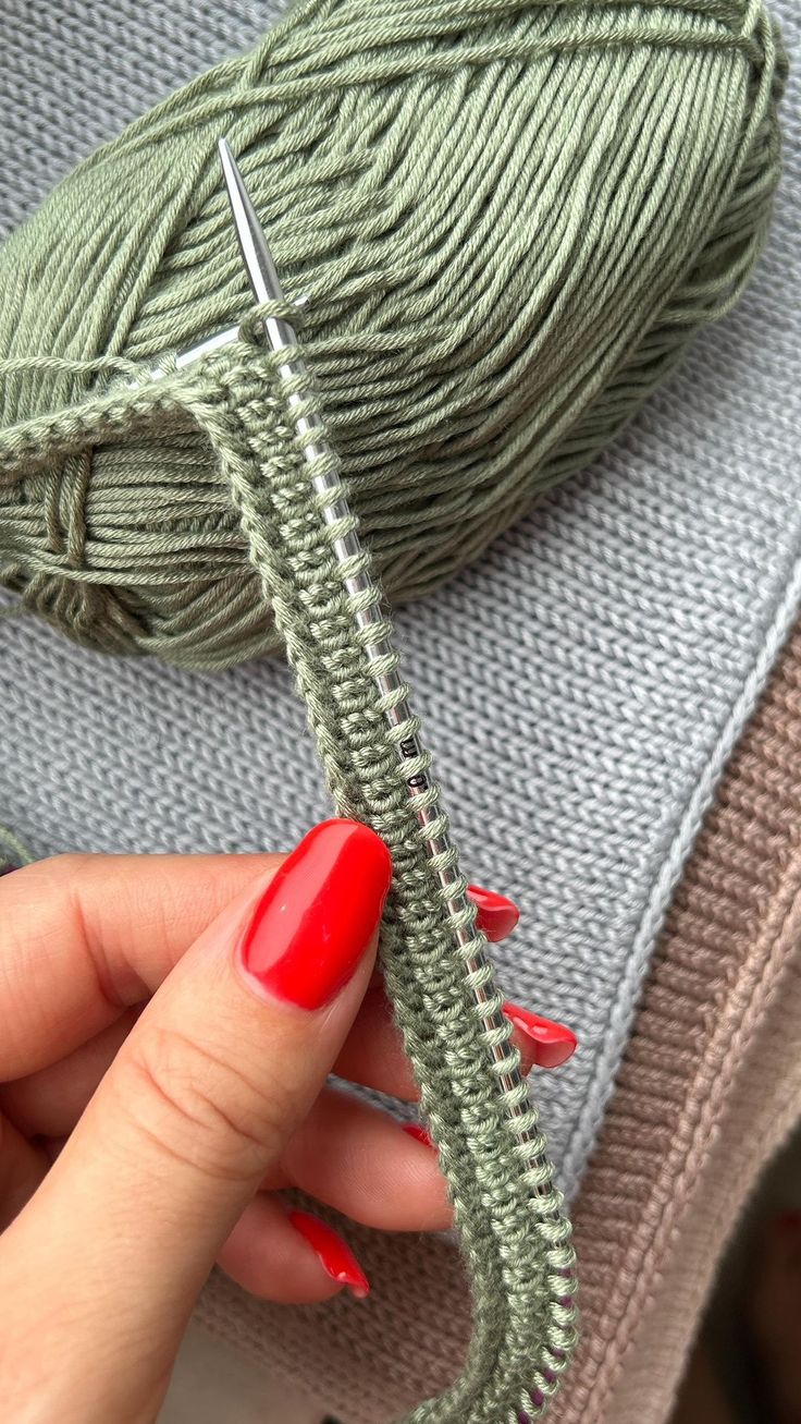 a woman's hand with red nail polish holding a green crochet hook