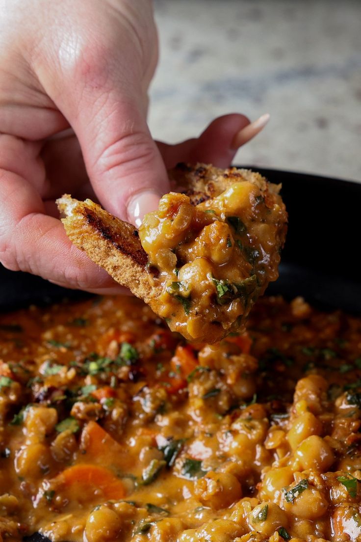 a person is dipping some kind of food into a pan filled with beans and vegetables