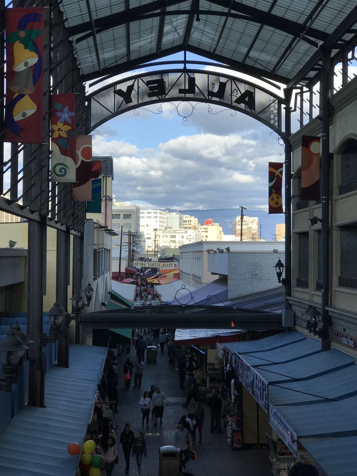 an outdoor market with lots of people walking around it and some buildings in the background