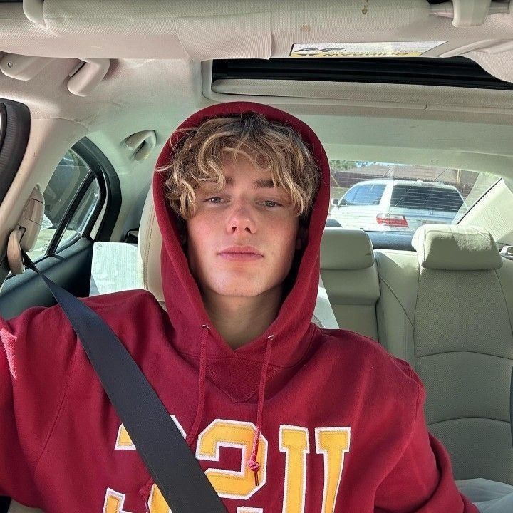 a young man sitting in the back seat of a car wearing a red hoodie