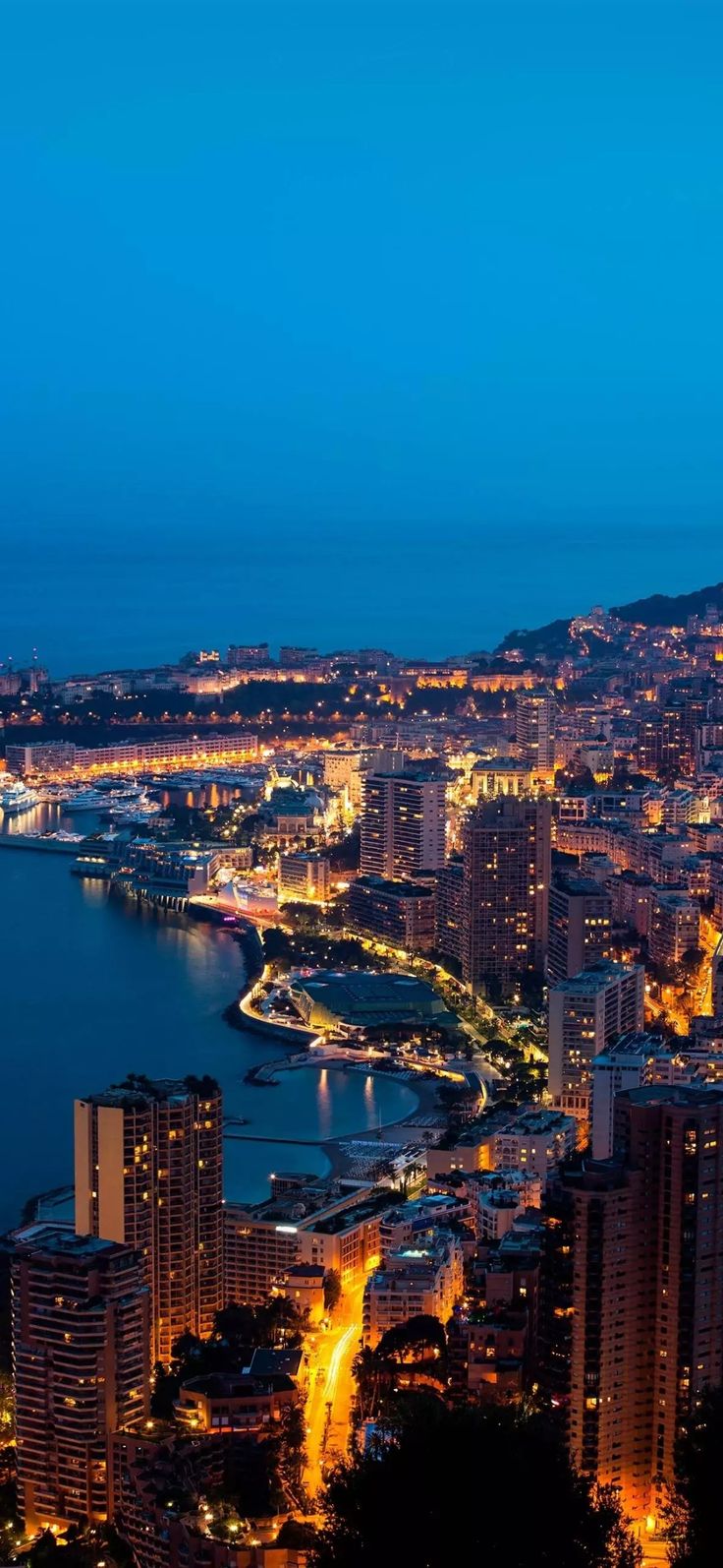 an aerial view of a city at night with lights on the buildings and water in the foreground