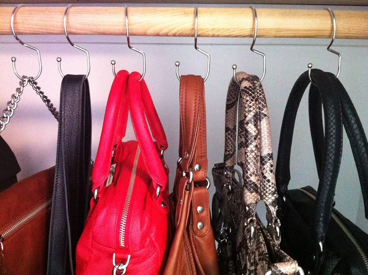 several purses are hanging on a rack in the closet, with one being held by a metal hook