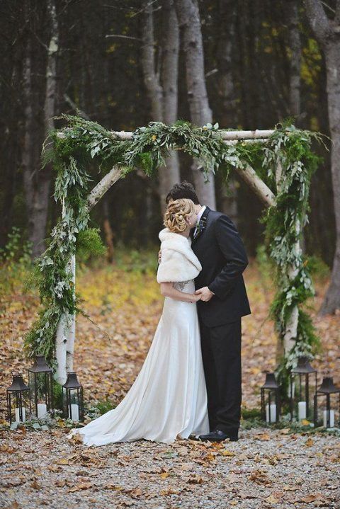 a bride and groom kissing under an arch made out of branches, surrounded by candles