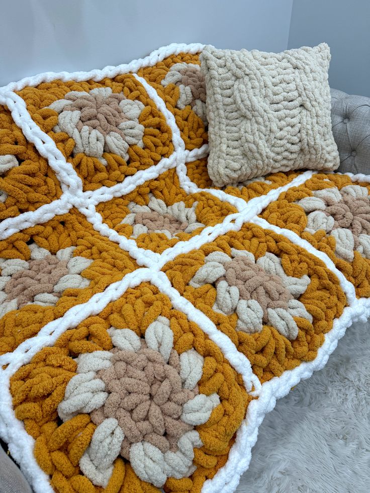 an orange and white crocheted blanket sitting on top of a bed next to two pillows