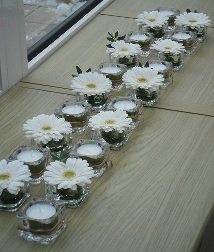 there are many candles with white flowers in them on the table next to each other