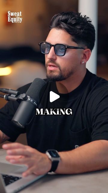 a man sitting at a table with a laptop and microphone in front of his face