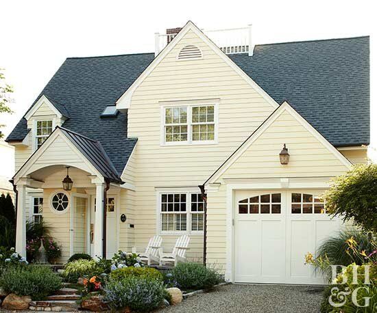 a white house with black shingles and lots of plants in front of the door