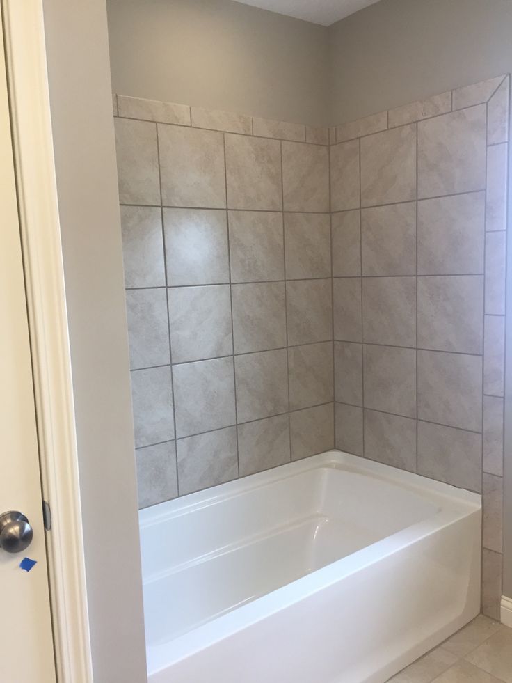 an empty bathroom with tiled walls and white tub in the corner, next to a door