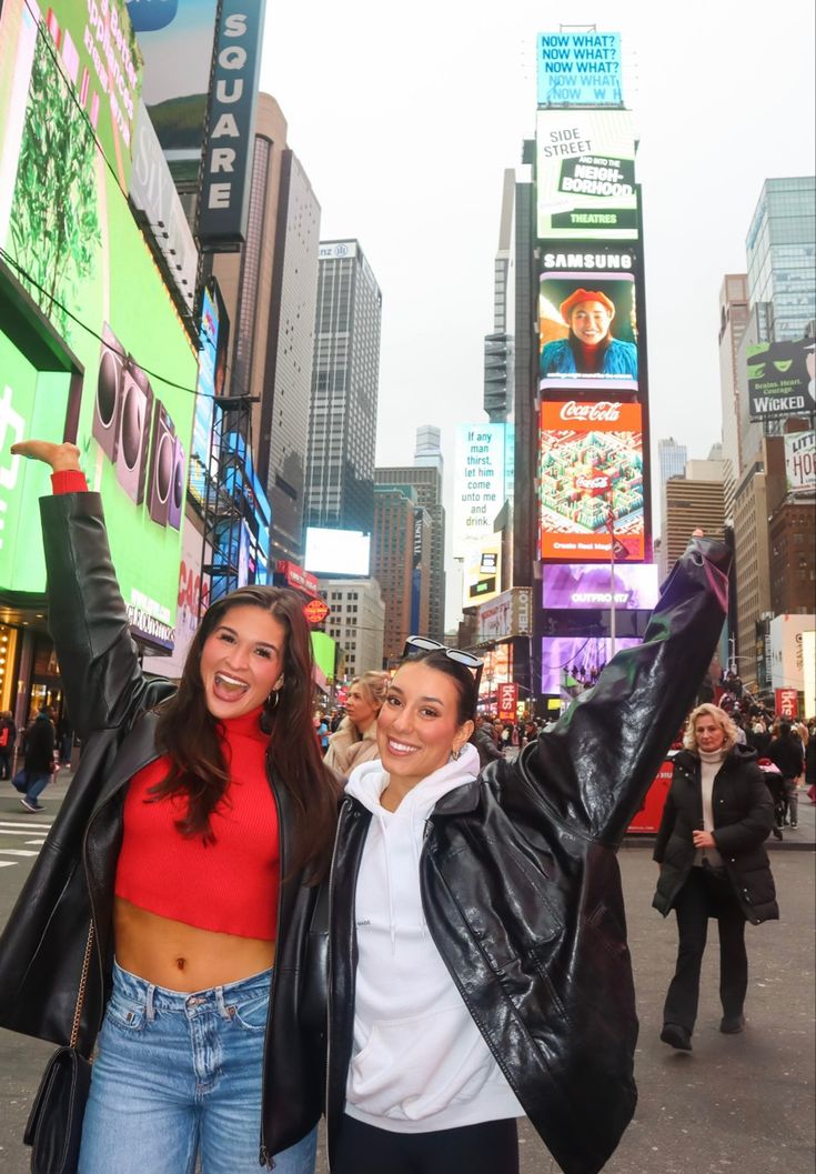 two women standing in the middle of a busy city street, one holding her arms up