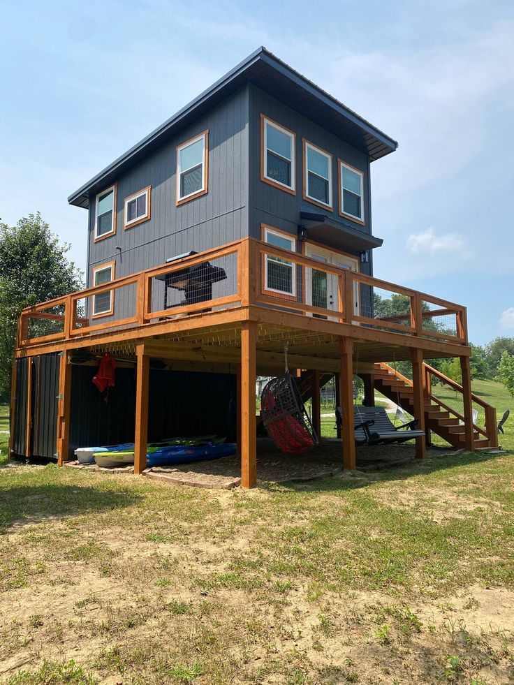 a two story house on stilts in the middle of a field with a boat parked under it