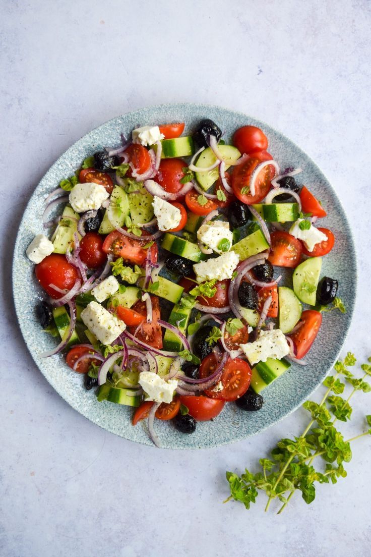 a salad with tomatoes, cucumbers, onions and olives on a blue plate