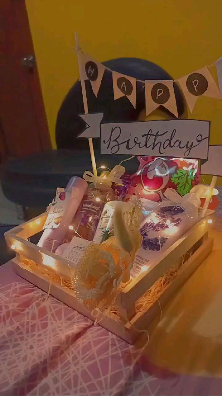 a birthday cake with candles and decorations in a wooden box on a pink table cloth