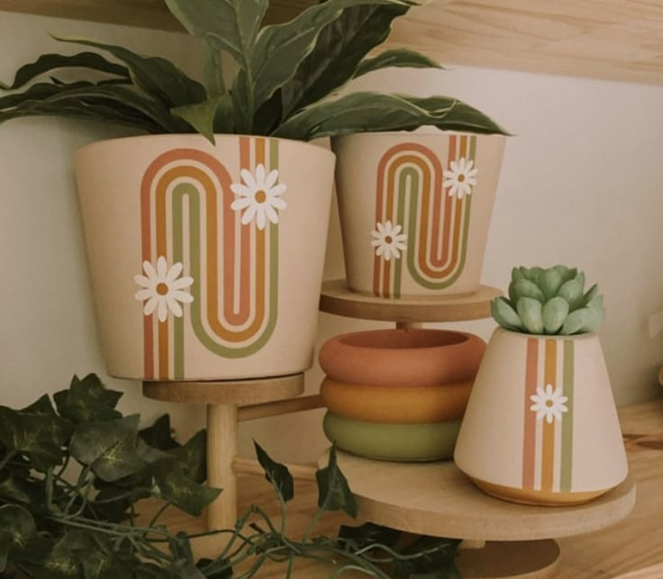 three flower pots sitting on top of a wooden shelf next to a potted plant