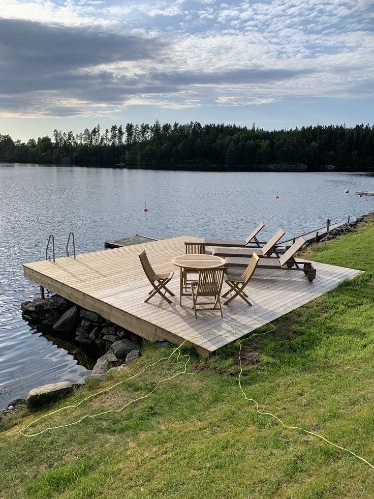 a wooden dock with chairs on it next to the water