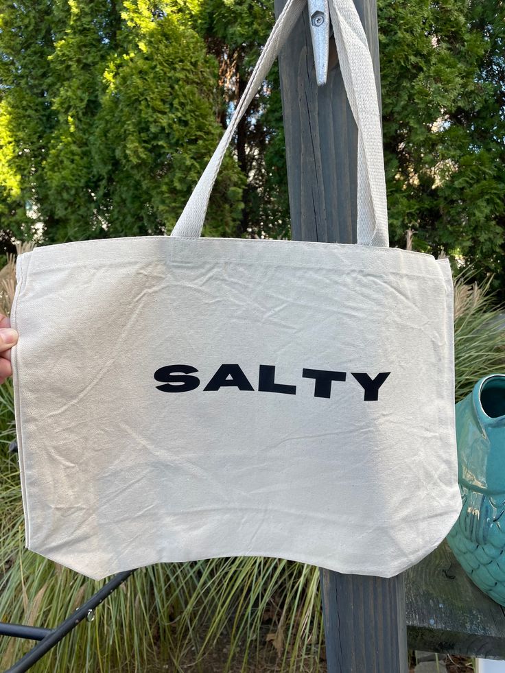 Stay salty no matter the season with the Salty Tote Bag! This extra large bag is perfect for carrying all the essentials — and then some. Bring it to the beach, farmer's market, campus, or run errands. This one can do it all and bring you beach style no matter where you go. Measures 20"W x 15"H x 5"D Large Capacity Cotton Bag For Beach Season, Everyday Cotton Shoulder Bag For Beach, Large Capacity Casual Canvas Beach Bag, Casual Large Capacity Canvas Beach Bag, Casual Large Canvas Beach Bag, Casual Large Capacity Canvas Bag For Beach Season, Cotton Shoulder Bag For Everyday Beach Use, Casual Cotton Beach Bag For Travel, Casual Cotton Beach Bags