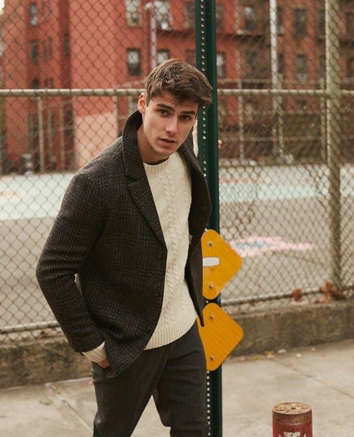 a young man leaning against a pole in front of a chain link fence and building