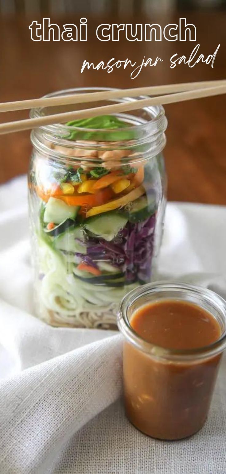 a mason jar filled with salad on top of a white cloth next to a wooden spoon